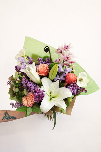 Bouquet of flowers with white lilies, pink roses, and purple hydrangeas on a light background