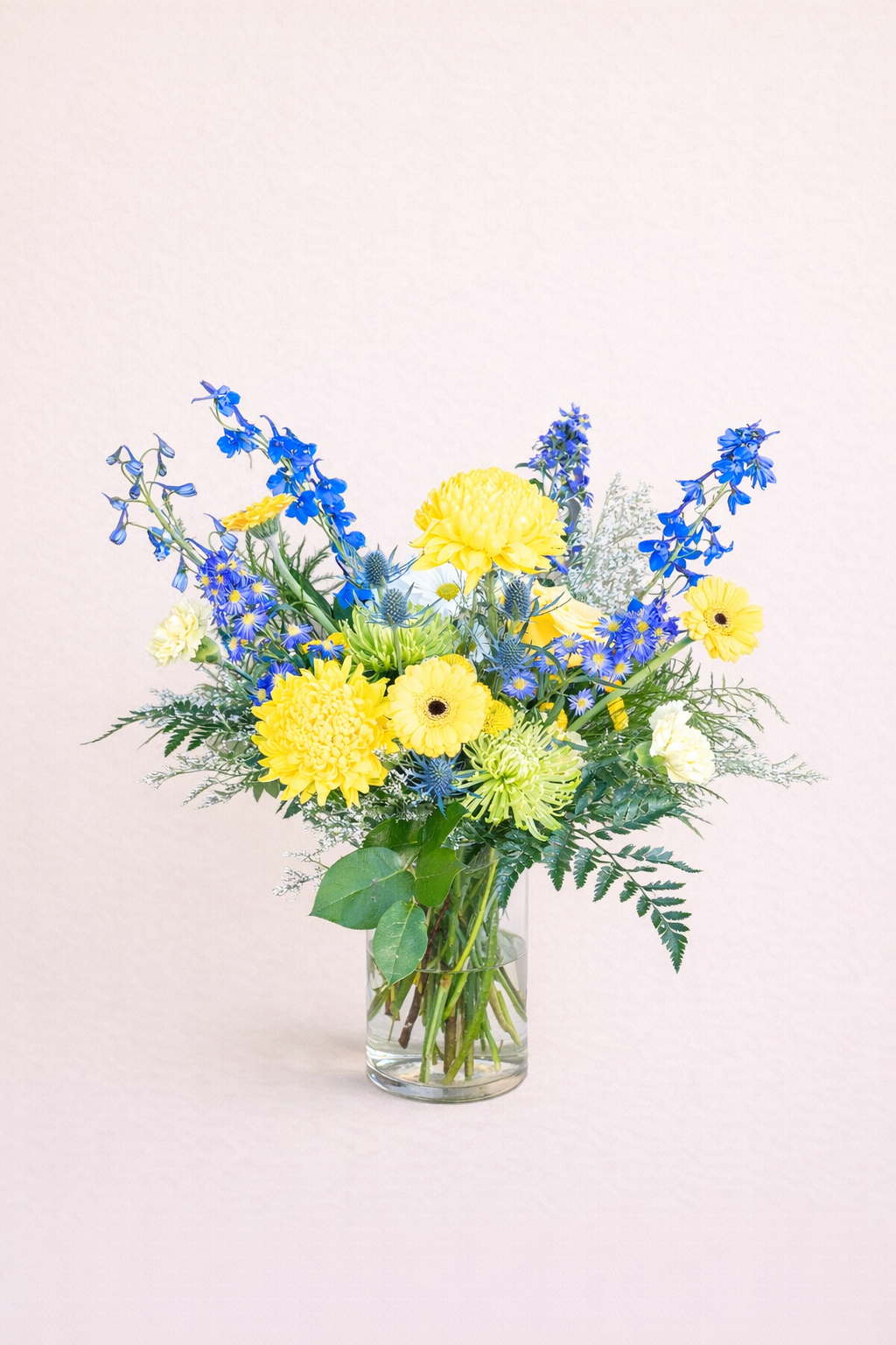 Bouquet of yellow and blue flowers in a clear vase on a light pink background