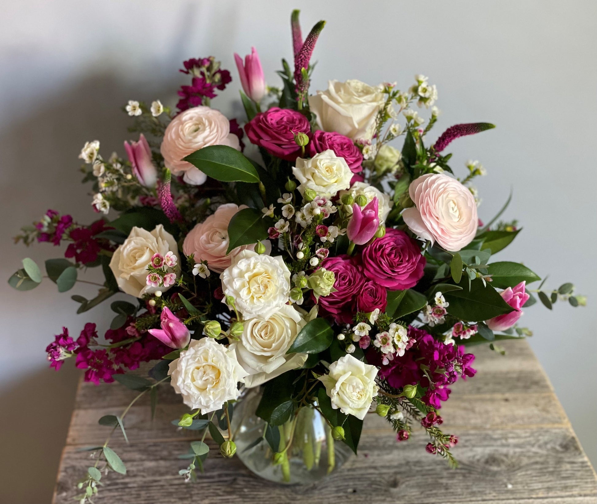 Bouquet of flowers in a clear vase on a wooden surface with a neutral background