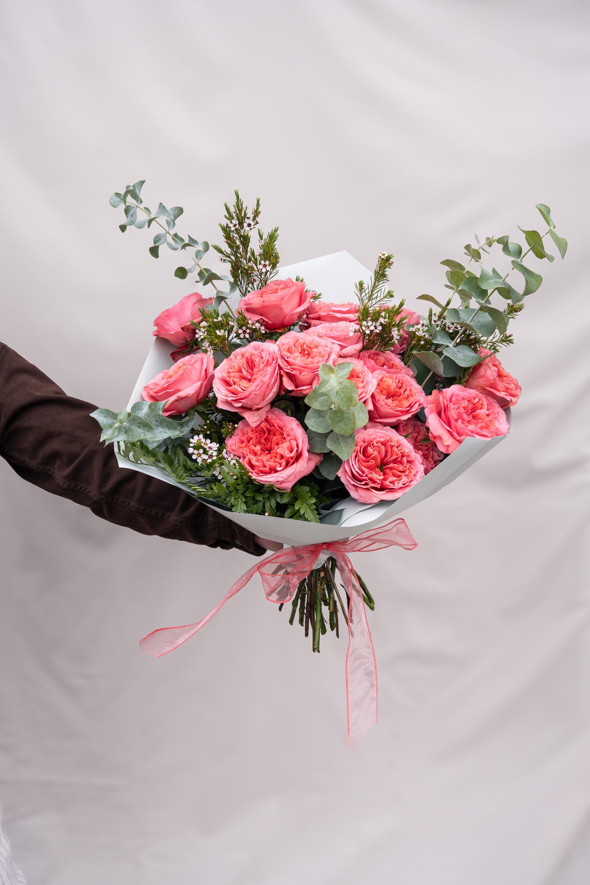 Bouquet of pink roses with greenery held by a gloved hand on a light background