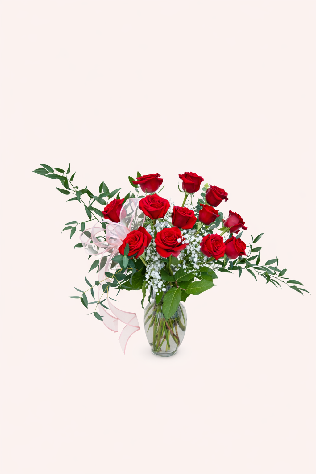 Bouquet of red roses with greenery in a clear vase on a light background