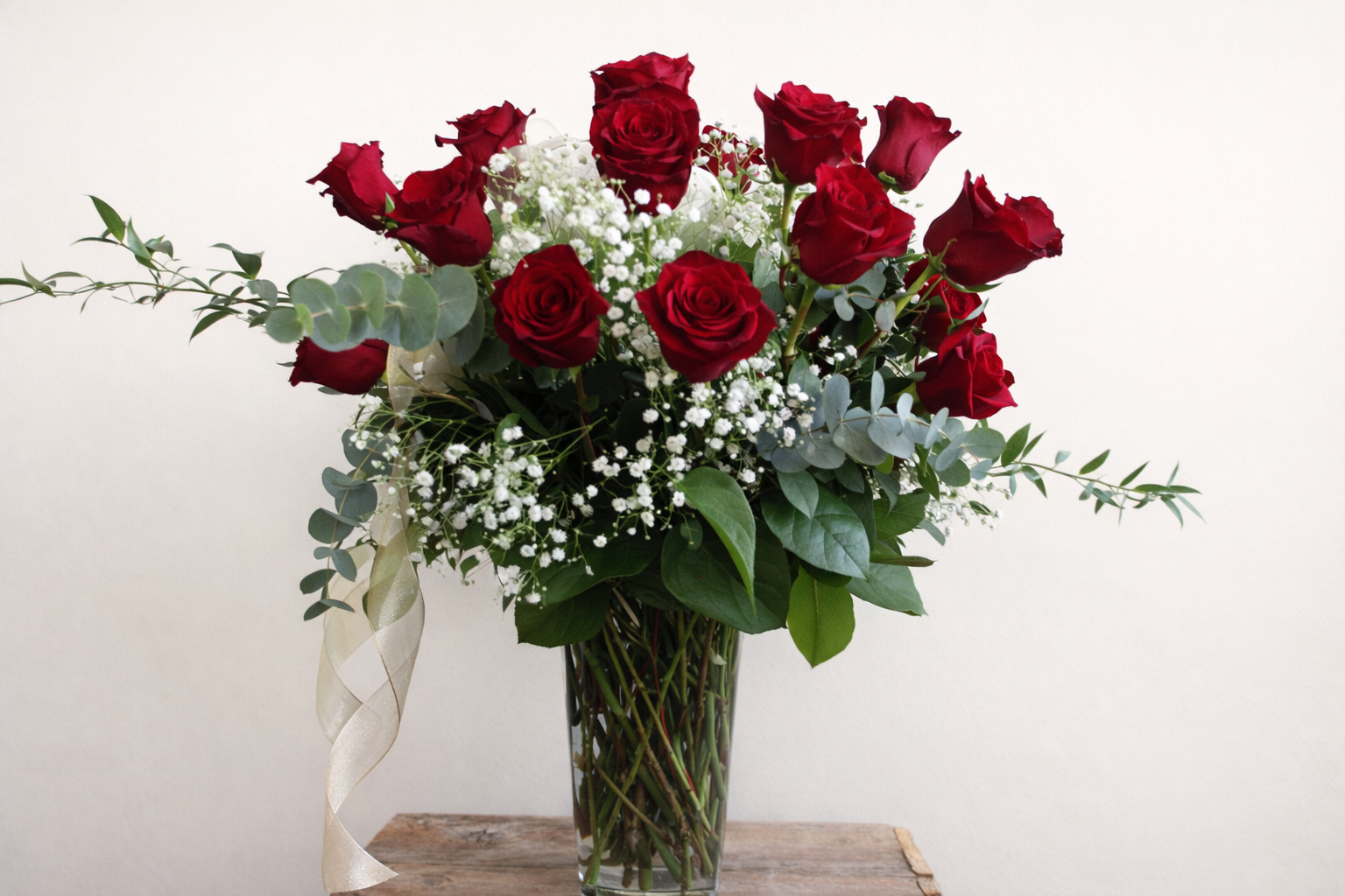 Bouquet of red roses with greenery in a clear vase on a wooden surface.