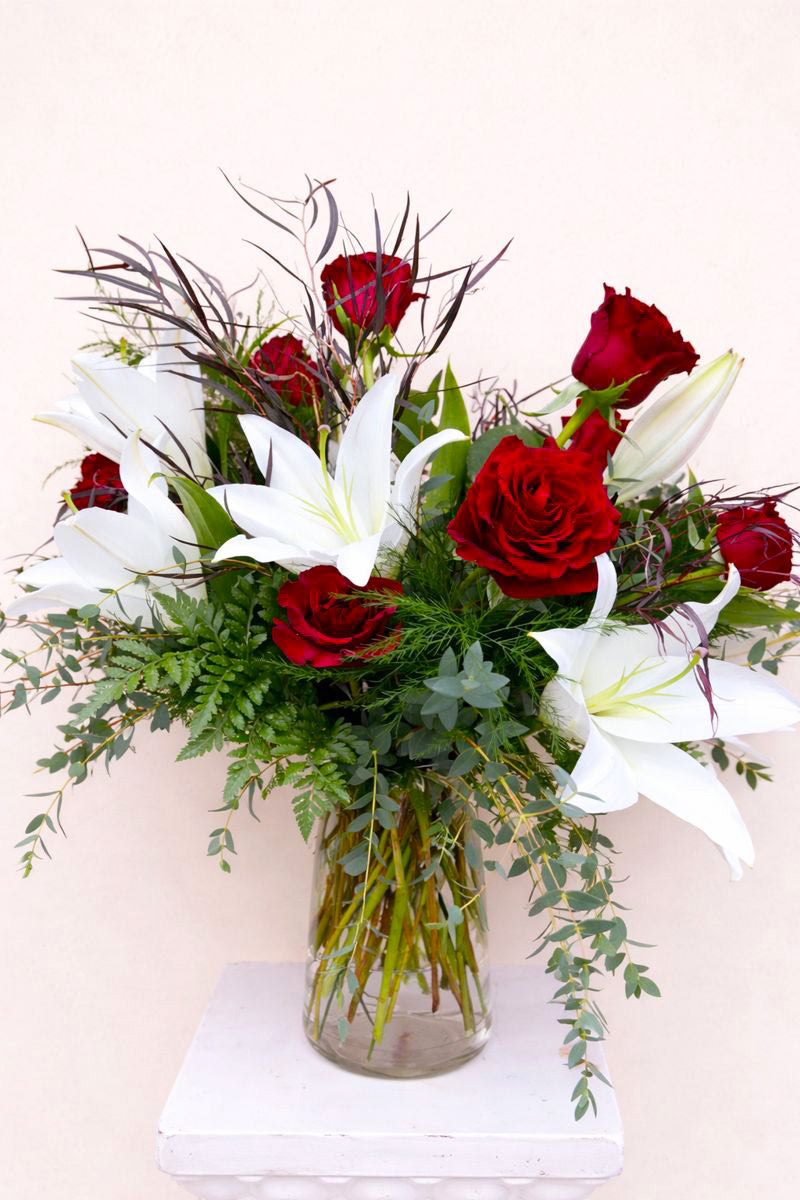 Bouquet of red roses and white lilies in a clear vase on a white background