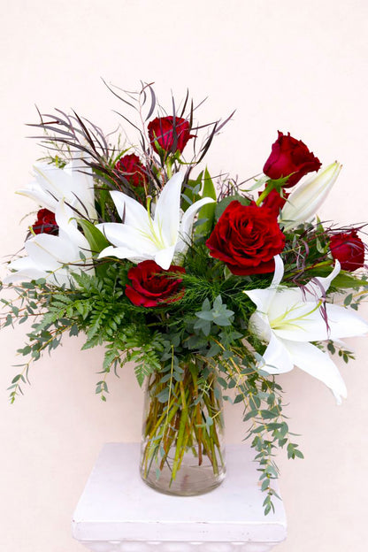 Bouquet of red roses and white lilies in a clear vase on a white background