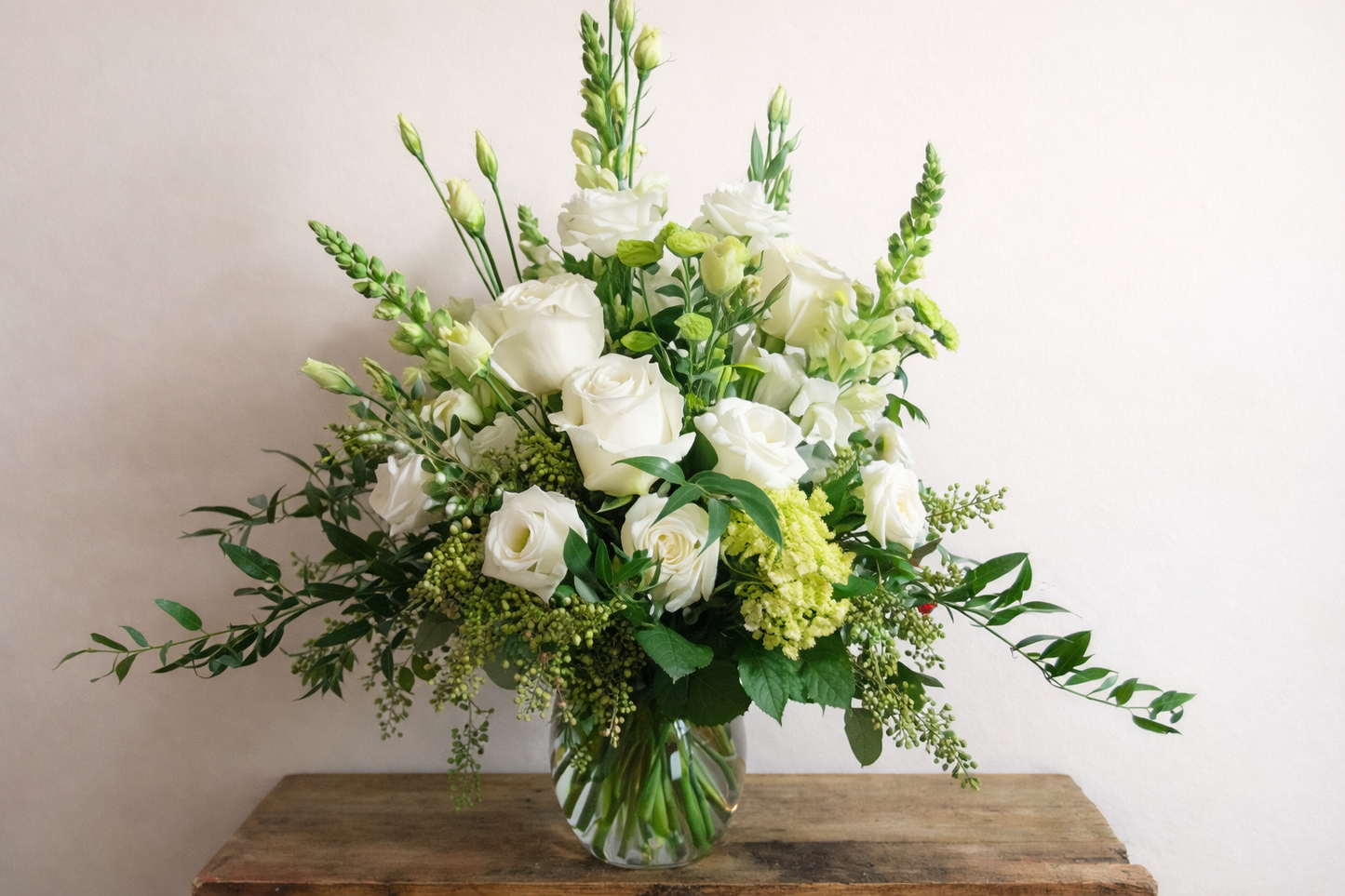 Bouquet of white and green flowers in a clear vase on a wooden table with a light background