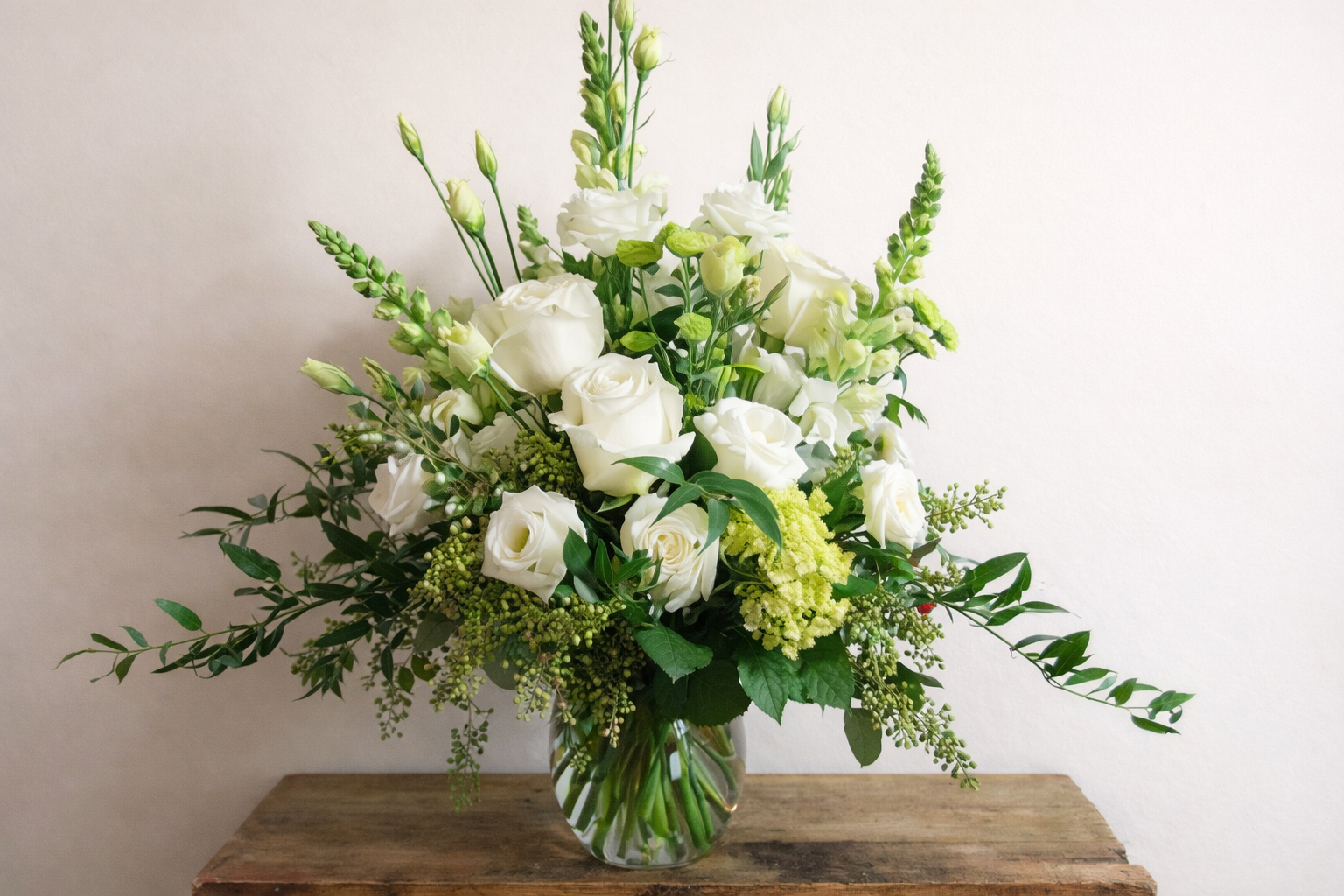 Bouquet of white and green flowers in a clear vase on a wooden table with a light background